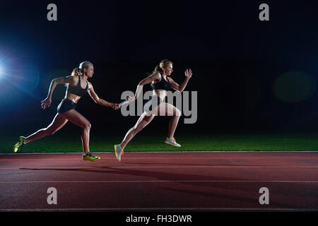 athletic runners passing baton in relay race Stock Photo