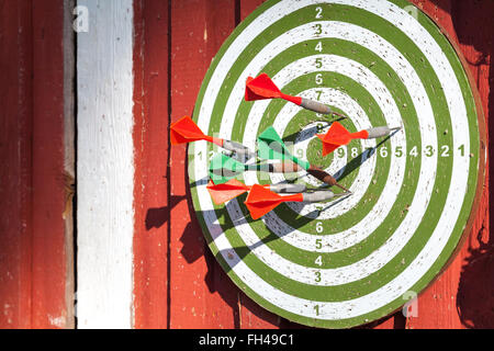 Darts target with many arrows hanging on red wooden wall Stock Photo