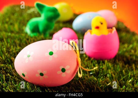 closeup of a pink decorated egg on the grass with some other colorful decorated eggs, a green easter rabbit and a toy chick emer