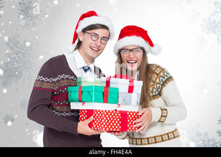 Composite image of portrait of smiling man and woman wearing santa hats and holding gifts Stock Photo