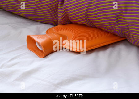 An orange rubber hot water bottle lying in a bed Stock Photo