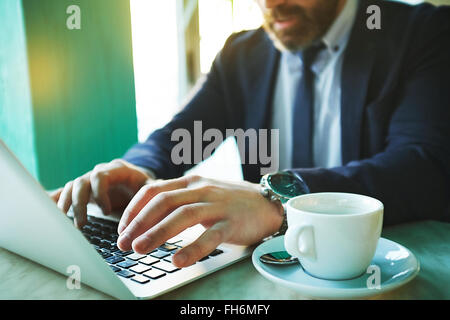 Hands of businessman typing with teacup near by Stock Photo