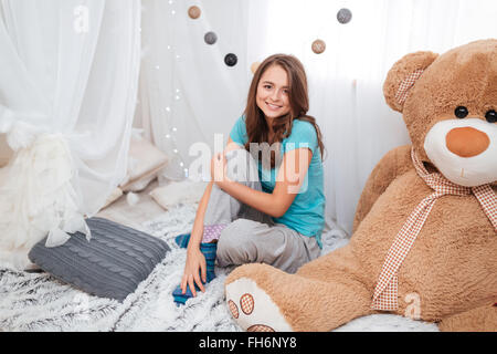 Cute cheerful girl with big plush bear sitting in children room at home Stock Photo