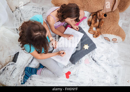 Top view of two lovely sisters sitting and colouring together in children room Stock Photo