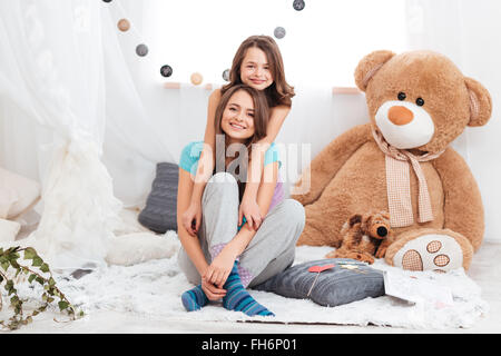 Two smiling beautiful sisters sitting together in children room Stock Photo