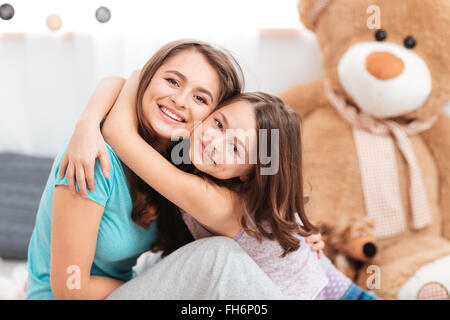 Two cheerful charming sisters smiling and embracing at home Stock Photo