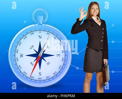 Girl holding leather briefcase in hand showing okay sign standing on background illustration of compass Stock Photo