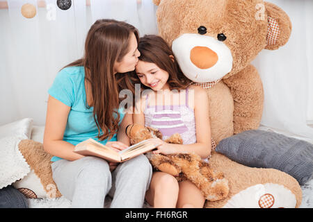 Two cute smiling sisters reading and kissing in children room Stock Photo