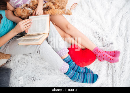 Closeup of beautiful legs of two young women sitting and reading a book on soft carpet Stock Photo