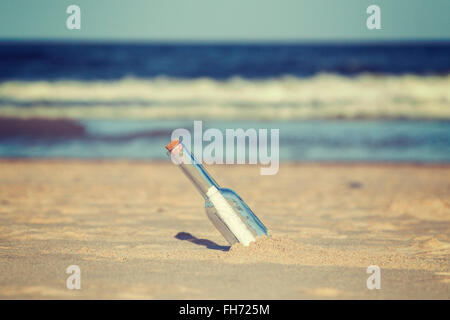 Vintage toned message in a bottle on beach, shallow depth of field. Stock Photo