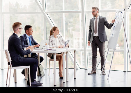 Group of young managers looking at businessman pointing at paper with data on whiteboard Stock Photo