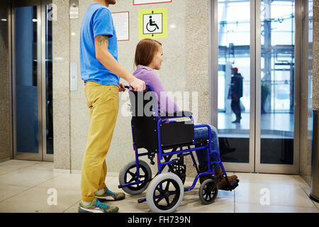 Guy and his girlfriend in wheelchair waiting for elevator Stock Photo
