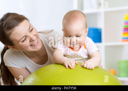 Mother with child doing exercises with green gymnastic ball at home. Concept of caring for the baby's health. Stock Photo