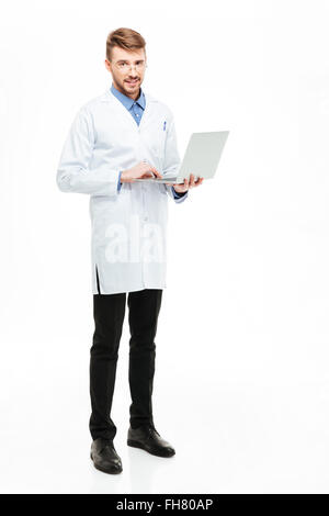 Full length portrait of a male doctor holding laptop computer and looking at camera isolated on a white background Stock Photo