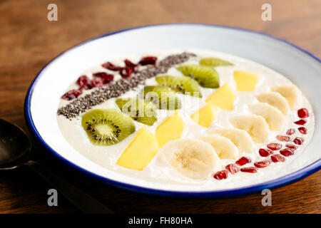 Banana smoothie bowl with kiwi, mango, banana, chia seeds, dried cranberries and pommegranate arils as topping. Stock Photo