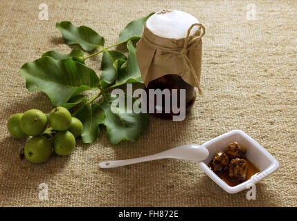 Jam jar nuts on textured burlap with leaves, fruit, white ceramic plate and spoon Stock Photo