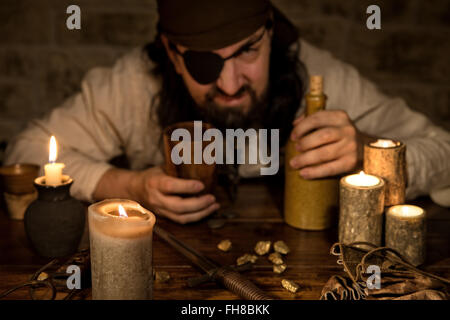 grumpy pirate with a bottle of rum sitting on a medieval table with a lot of candles Stock Photo