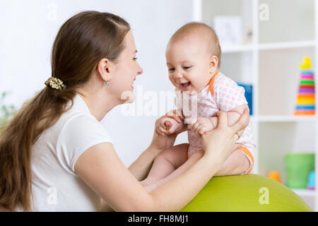Happy mother with kid doing exercises with green gymnastic ball at home. Concept of caring for the baby's health. Stock Photo