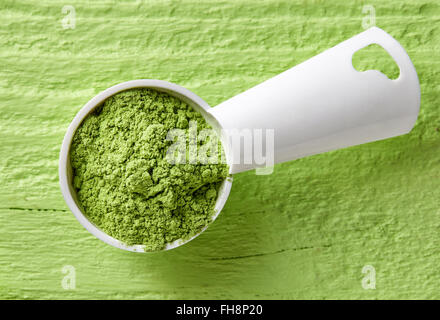 Measuring scoop of barley or wheat grass powder on green table, top view Stock Photo