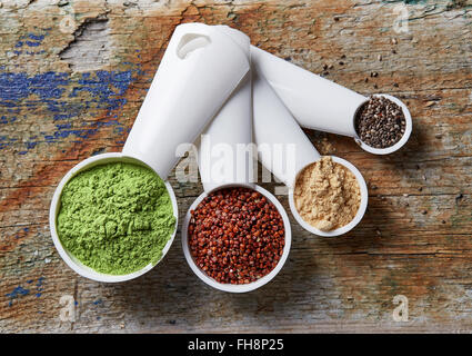 Measuring scoops with barley or wheat grass powder, red quinoa, maca powder and chia seeds on wooden table, top view Stock Photo