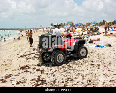 Miami, Florida, USA - May 28, 2007: A mounted policeman of his quad-bike red, stops at the beach communicating something to some Stock Photo