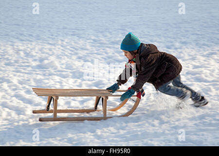 Little boy pushing sled uphills in the snow Stock Photo