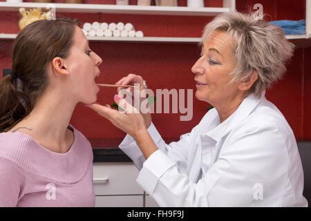 female experienced doctor with throat depressor and younger patient, in doctors office Stock Photo