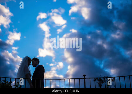Silhouette of young bridal couple standing face to face in front of a cloudy sky Stock Photo