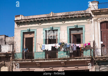 Daily life in Cuba - Cuban man with clothes pegs on t-shirt leaning on balcony railings with washing on line drying at Havana, Cuba, West Indies Stock Photo