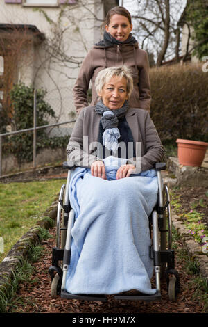 daughter cares about mother in a wheelchair, outdoors in a park Stock Photo