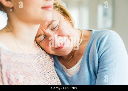 Senior woman with closed eyes leaning against young woman's shoulder