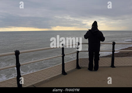 Worthing Pier, West Sussex, England, UK. 24th February 2016.  While much of England saw blue skies and sunshine, on the south coast it was overcast with dramatic clouds over the English Channel. Man wrapped up against the cold looks out to sea. Credit:  Julia Gavin UK/Alamy Live News Stock Photo