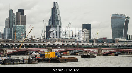 Prominent yellow container on a barge moored in the centre of the River Thames with tall iconic glass towerblocks and bridge Stock Photo