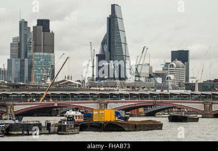 Prominent yellow container on a barge moored in the centre of the River Thames with tall iconic glass towerblocks and bridge Stock Photo