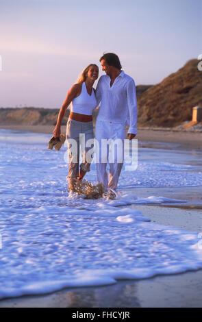 Couple in love enjoying romantic walk through beach waves along California shore at sunset Stock Photo