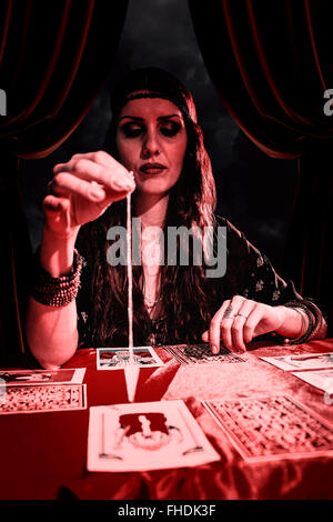 Composite image of female fortune teller looking at pendulum Stock Photo