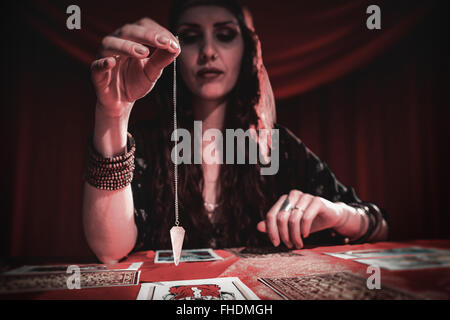 Composite image of female fortune teller holding pendulum with eyes closed Stock Photo