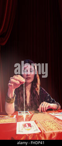 Composite image of female fortune teller looking at pendulum Stock Photo