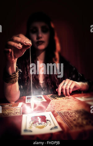 Composite image of female fortune teller using pendulum Stock Photo