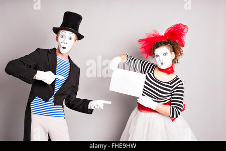 Portrait of happy smiling young actors showing blank signboard, with copyspace area for text or slogan, against grey background Stock Photo