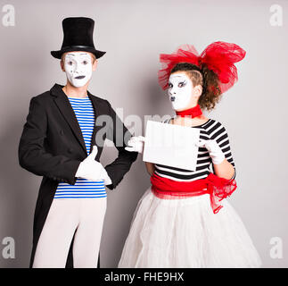 Portrait of happy smiling young actors showing blank signboard, with copyspace area for text or slogan, against grey background Stock Photo