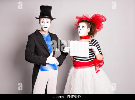 Portrait of happy smiling young actors showing blank signboard, with copyspace area for text or slogan, against grey background Stock Photo