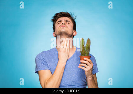 concept with a young man in T-shirt, holding in hand a cactus suggesting pain Stock Photo