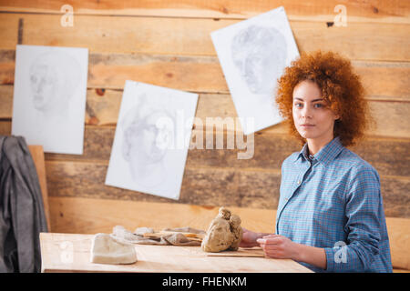 Beautiful redhead woman potter sitting and working with clay in workshop Stock Photo