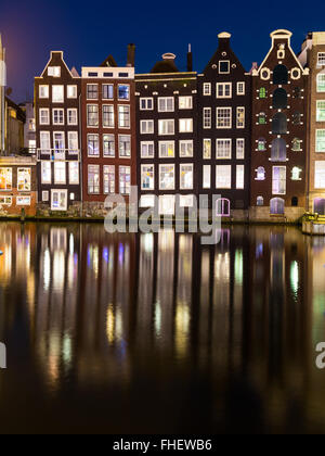 Old Buildings along the Damrak in Amsterdam at night. Reflections can be seen in the water. Stock Photo