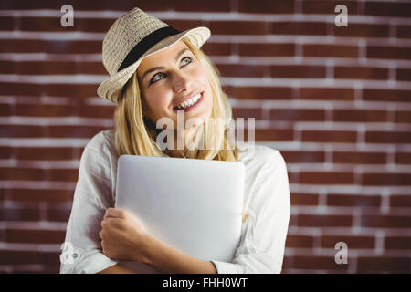 Beautiful blonde woman holding laptop against her chest Stock Photo