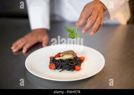 Chef putting basil leaf on spaghetti dish Stock Photo
