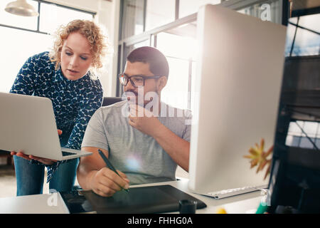 Shot of two designers working in their office using a laptop, digital graphics tablet and desktop computer. Man sitting at his d Stock Photo