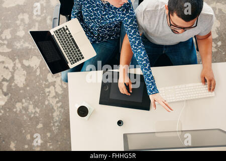 Top vie of a woman designer showing something on desktop monitor to man working graphics tablet and pc. Young graphic designers Stock Photo