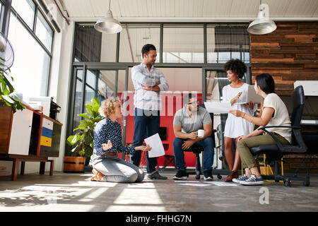 Creative team having a discussion on new design project in office. Project plan laid on floor with coworkers meeting and discuss Stock Photo